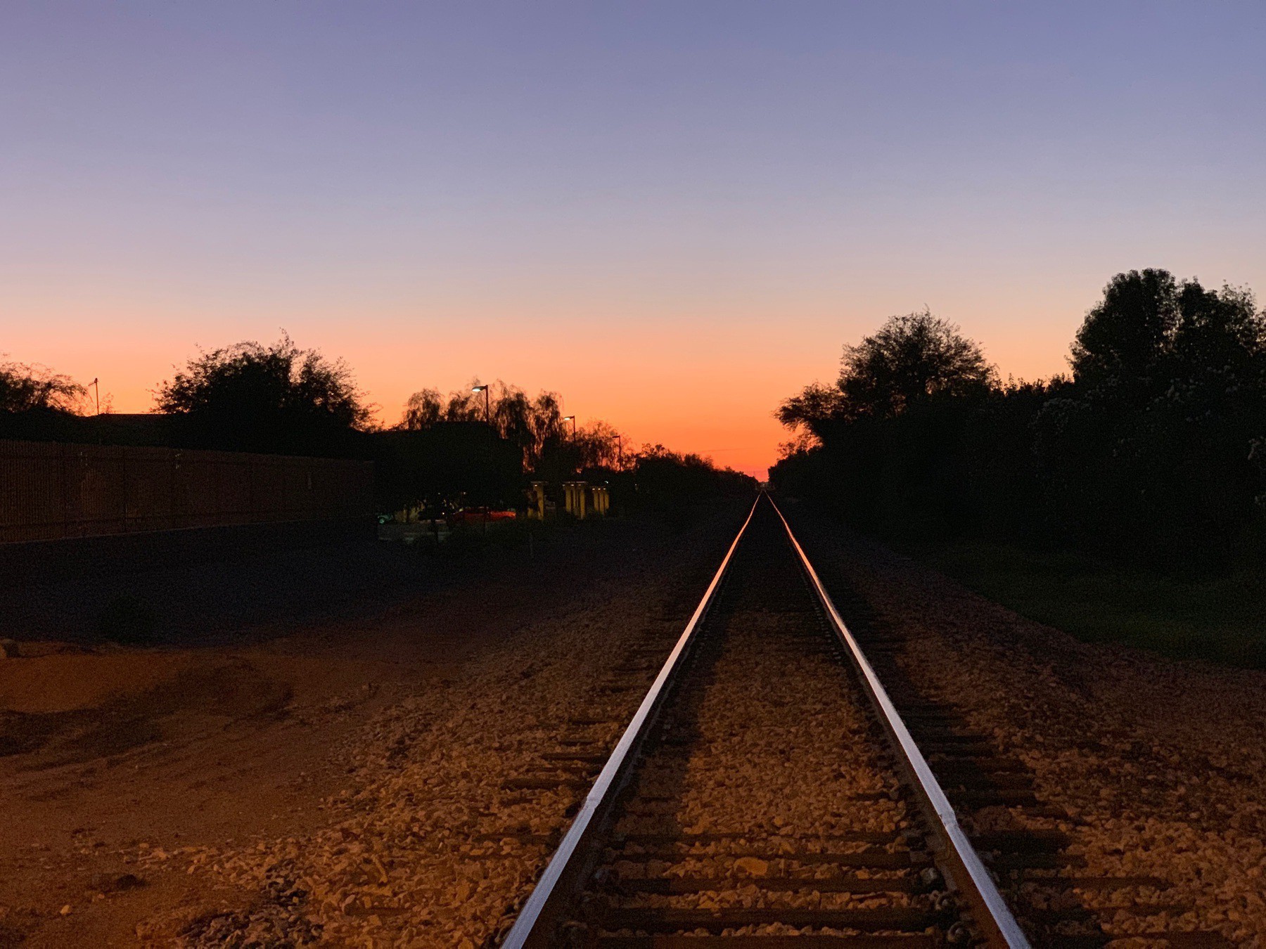 Two railroad tracks converging into a desert sunset